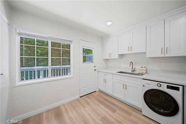 clothes washing area with cabinets, light hardwood / wood-style floors, washer / dryer, and sink