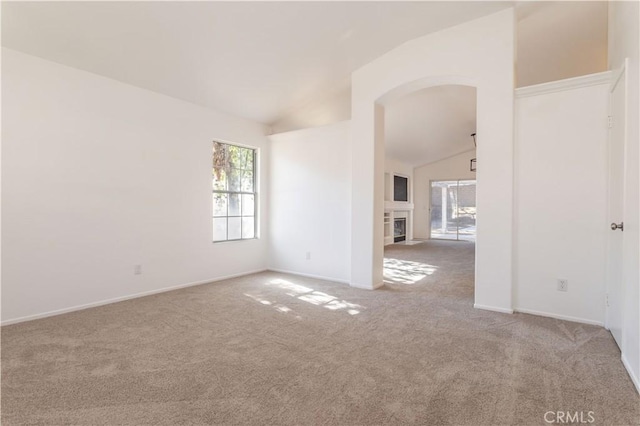 carpeted spare room featuring a fireplace, vaulted ceiling, and a wealth of natural light