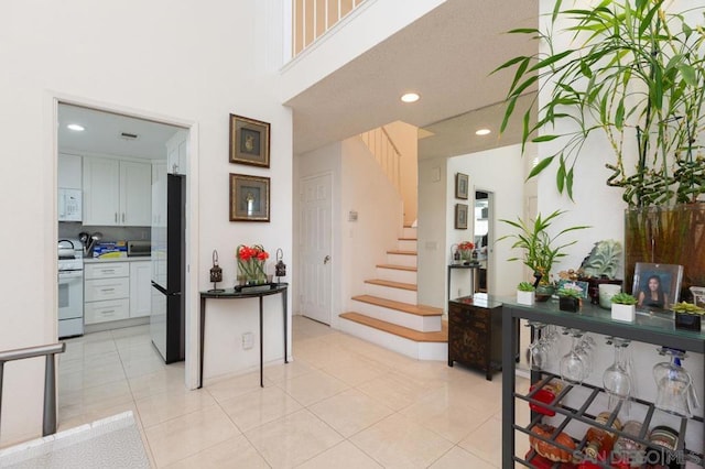 kitchen with white appliances, light tile patterned floors, a high ceiling, and white cabinets