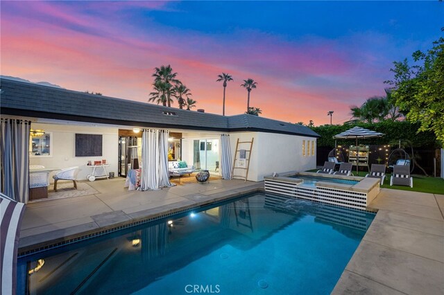 pool at dusk featuring a jacuzzi and a patio area