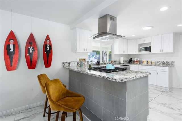 kitchen with appliances with stainless steel finishes, a kitchen breakfast bar, kitchen peninsula, island exhaust hood, and white cabinets