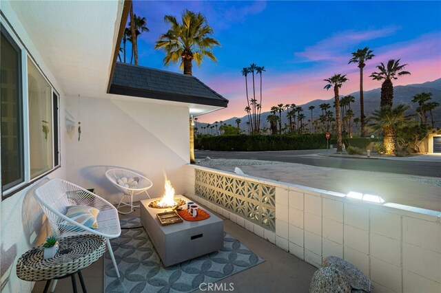 balcony at dusk featuring a mountain view, a patio area, and an outdoor fire pit