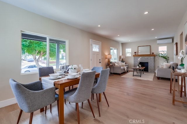 dining space featuring a wall mounted air conditioner, light hardwood / wood-style flooring, and a tile fireplace