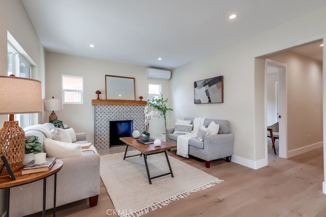 living room with light hardwood / wood-style flooring, a wall unit AC, and a tile fireplace