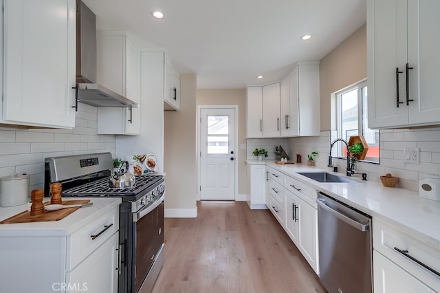 kitchen with white cabinetry, sink, stainless steel appliances, and wall chimney exhaust hood