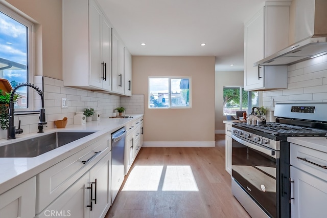 kitchen with white cabinetry, appliances with stainless steel finishes, sink, and wall chimney range hood