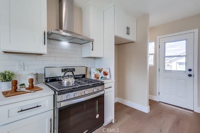 kitchen with stainless steel gas range oven, light hardwood / wood-style flooring, white cabinets, wall chimney range hood, and backsplash