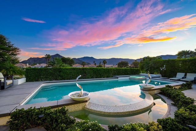 pool at dusk featuring an in ground hot tub, a mountain view, and a patio