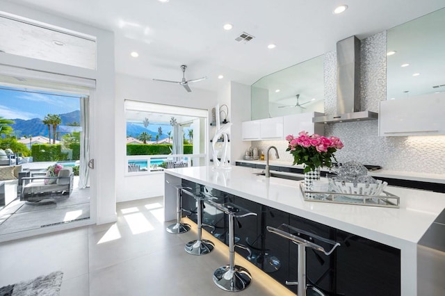 kitchen with white cabinetry, sink, backsplash, ceiling fan, and wall chimney exhaust hood