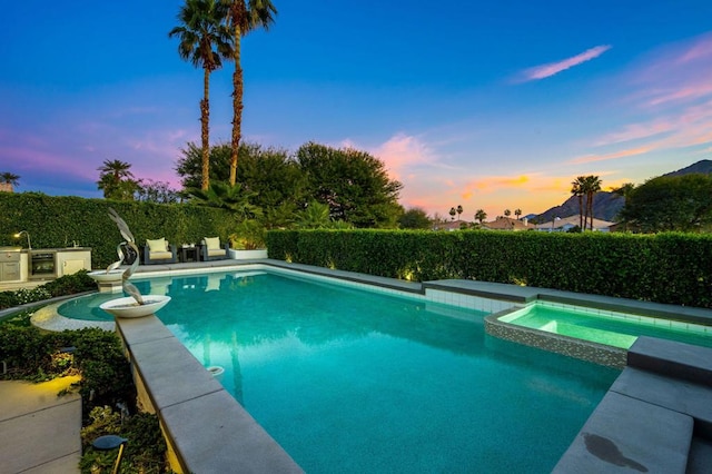 pool at dusk featuring an in ground hot tub and an outdoor kitchen