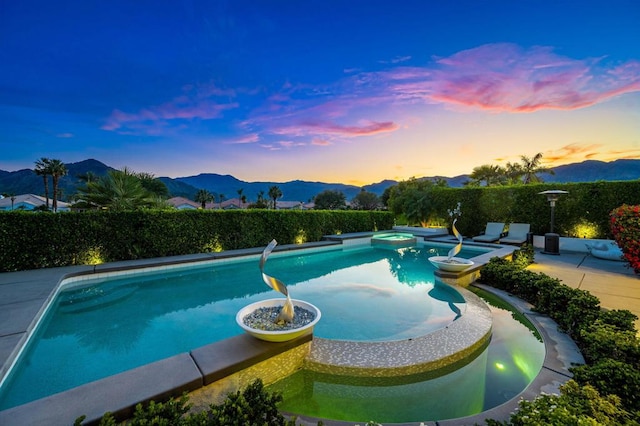 pool at dusk featuring a mountain view, a patio, and an in ground hot tub