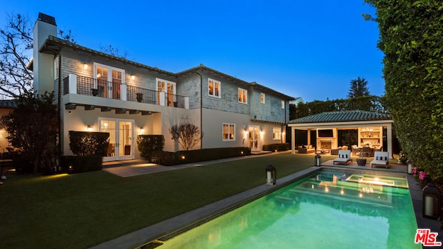 back house at dusk featuring a balcony, an outdoor hangout area, and a patio area