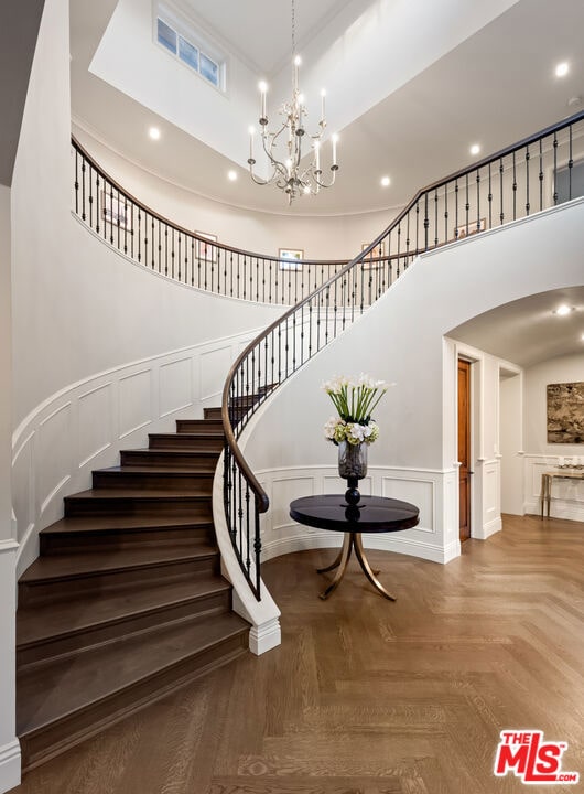 stairway with a towering ceiling, parquet floors, and a chandelier