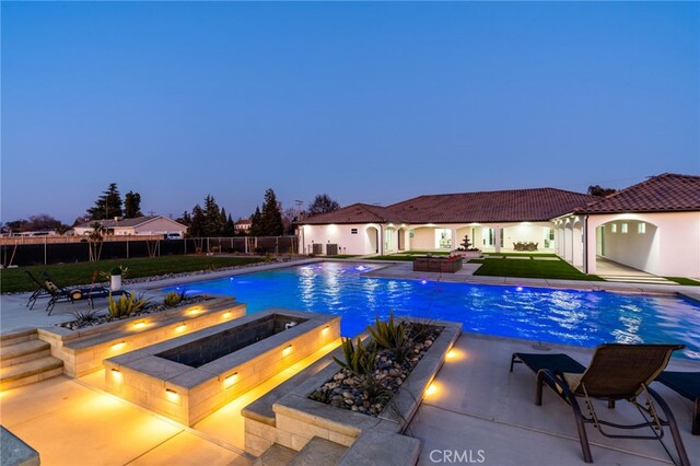 pool at dusk with an in ground hot tub and a patio