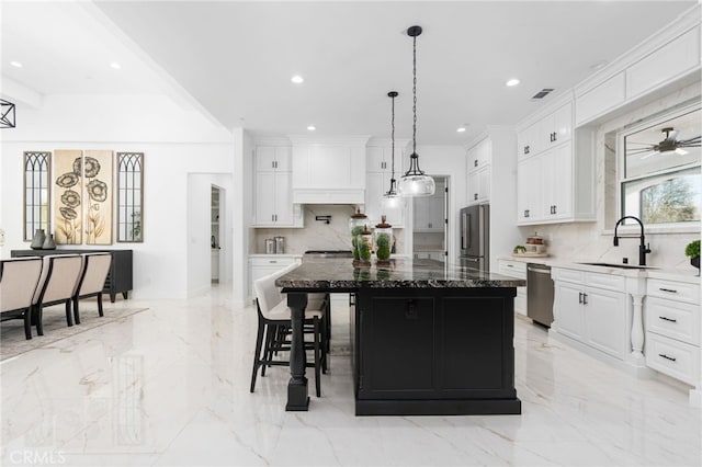 kitchen with a kitchen island, appliances with stainless steel finishes, white cabinetry, sink, and dark stone countertops