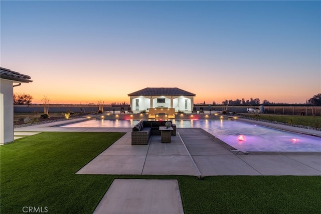 pool at dusk featuring a patio, an outbuilding, and a lawn