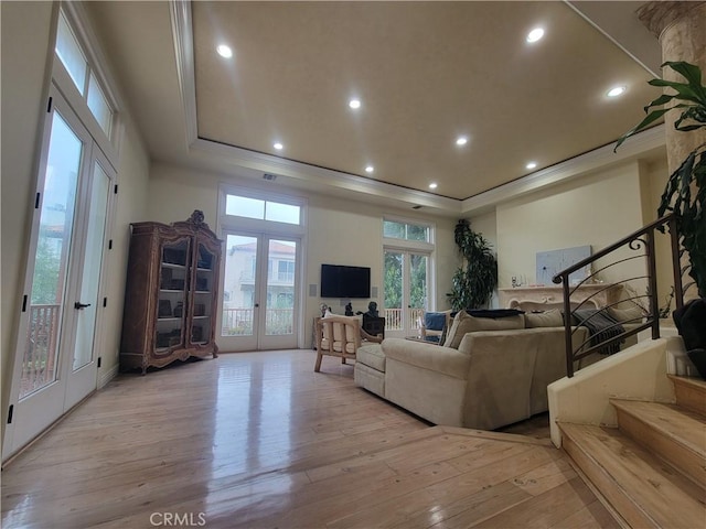 living room featuring french doors, a tray ceiling, crown molding, and light wood-type flooring