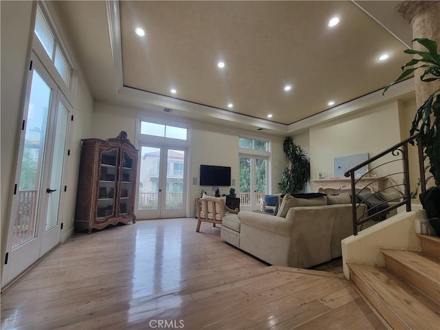 living area featuring french doors, light wood-style flooring, a tray ceiling, and stairs