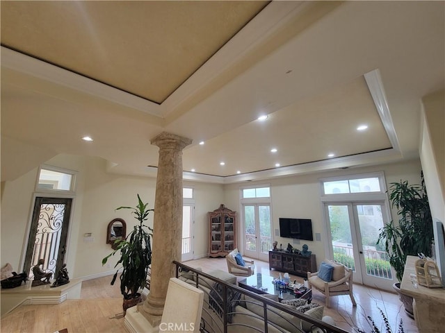 living room with french doors, ornate columns, ornamental molding, a tray ceiling, and light hardwood / wood-style floors