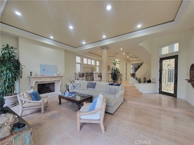 living room with crown molding, a raised ceiling, decorative columns, and light wood-type flooring