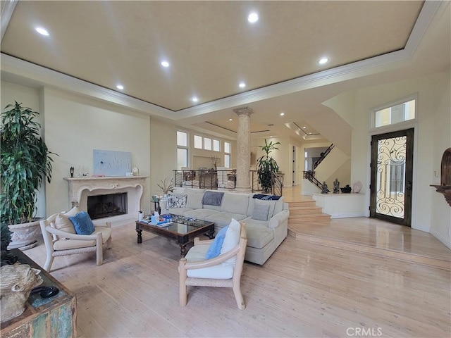 living room with crown molding, ornate columns, a raised ceiling, light wood-style floors, and a fireplace