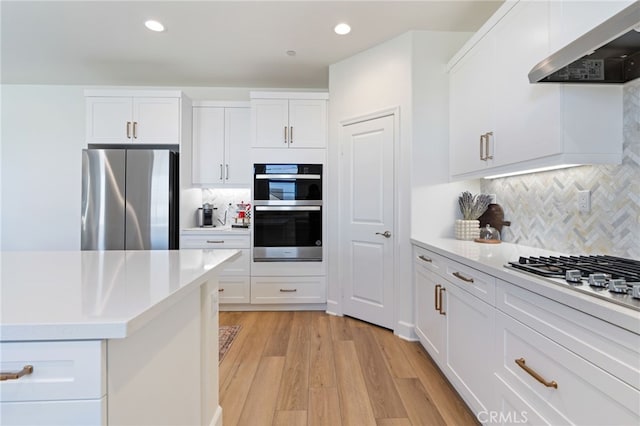 kitchen with light hardwood / wood-style flooring, appliances with stainless steel finishes, white cabinetry, decorative backsplash, and custom exhaust hood