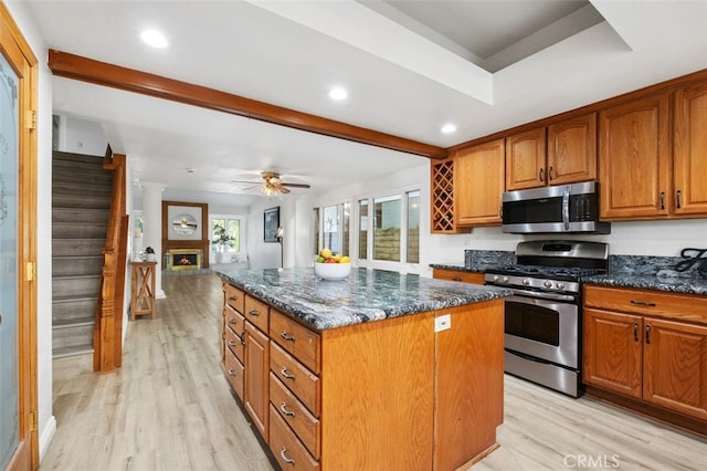 kitchen with appliances with stainless steel finishes, a center island, light wood-type flooring, and dark stone counters