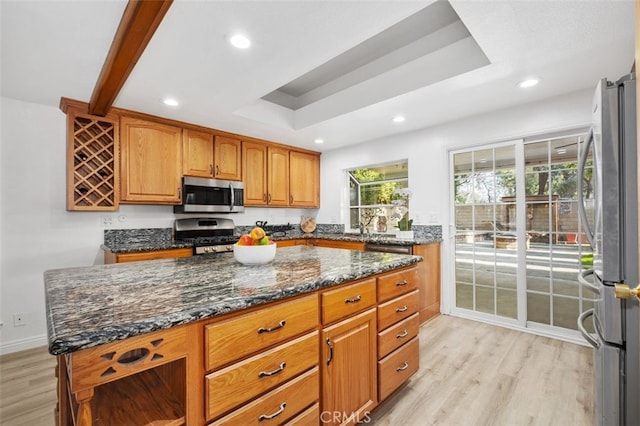 kitchen with appliances with stainless steel finishes, dark stone countertops, a tray ceiling, a kitchen island, and light wood-type flooring