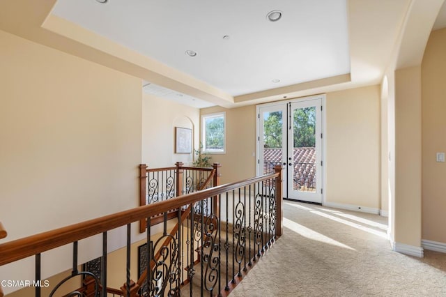 corridor with french doors, a raised ceiling, and carpet