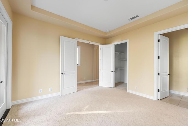 unfurnished bedroom with a walk in closet, light colored carpet, and a closet