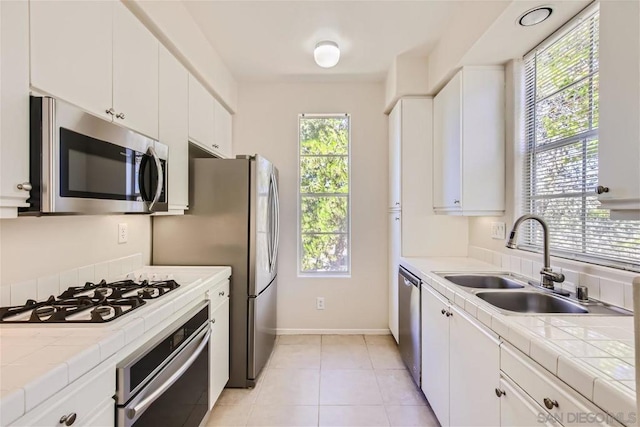 kitchen with stainless steel appliances, sink, tile counters, and white cabinets