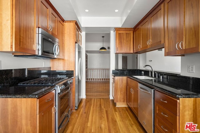 kitchen with sink, dark stone counters, hanging light fixtures, stainless steel appliances, and light hardwood / wood-style flooring