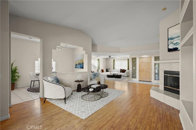 living room featuring a tile fireplace, vaulted ceiling, ceiling fan, and light hardwood / wood-style flooring