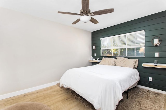 bedroom featuring hardwood / wood-style floors, ceiling fan, and wood walls