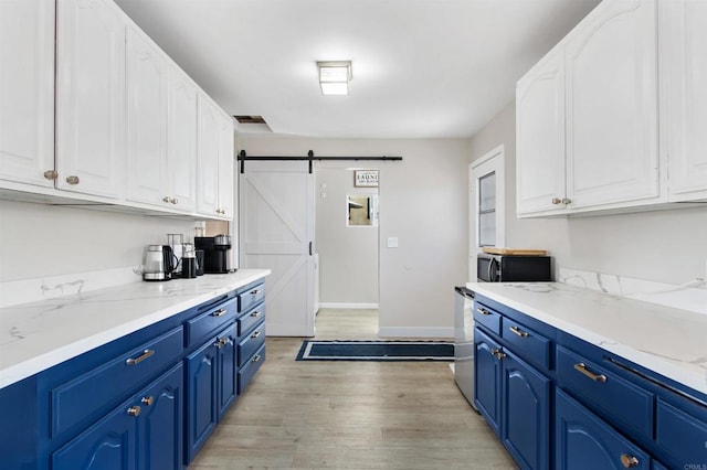 kitchen with blue cabinetry, light stone countertops, white cabinets, a barn door, and light wood-type flooring