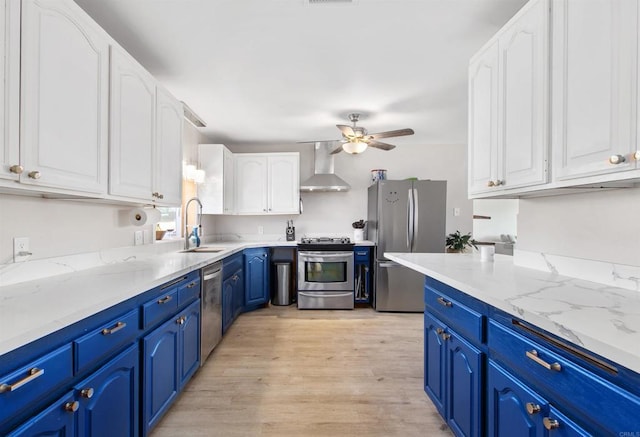 kitchen featuring blue cabinetry, white cabinetry, stainless steel appliances, and wall chimney range hood