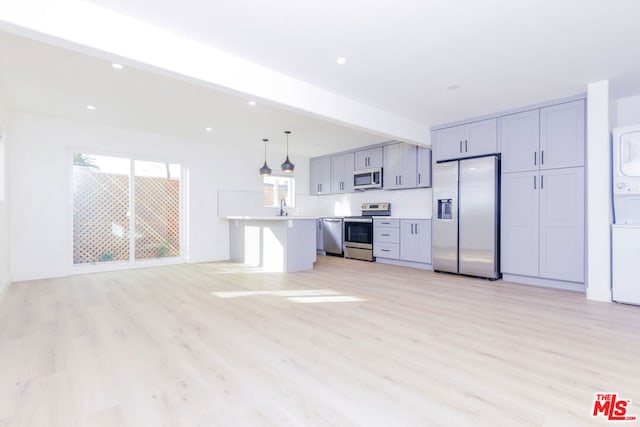 kitchen with pendant lighting, light hardwood / wood-style flooring, stainless steel appliances, stacked washer and clothes dryer, and a center island