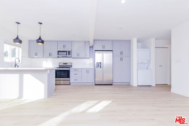 kitchen with stacked washer and dryer, appliances with stainless steel finishes, gray cabinets, and pendant lighting