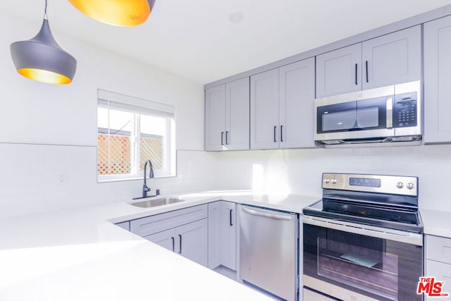 kitchen featuring sink, gray cabinetry, backsplash, hanging light fixtures, and stainless steel appliances