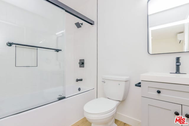 full bathroom featuring bath / shower combo with glass door, hardwood / wood-style floors, vanity, and toilet