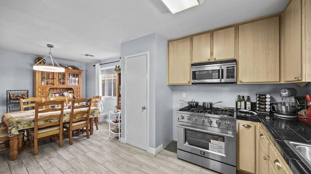 kitchen featuring appliances with stainless steel finishes, light wood-type flooring, light brown cabinetry, and decorative light fixtures