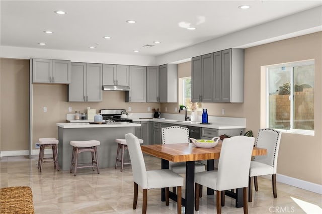 kitchen with under cabinet range hood, range with gas cooktop, light countertops, and gray cabinetry