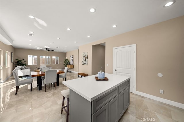 kitchen with recessed lighting, gray cabinetry, a kitchen island, baseboards, and light countertops