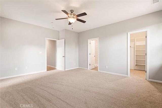 unfurnished bedroom featuring ceiling fan, a walk in closet, light colored carpet, and ensuite bath