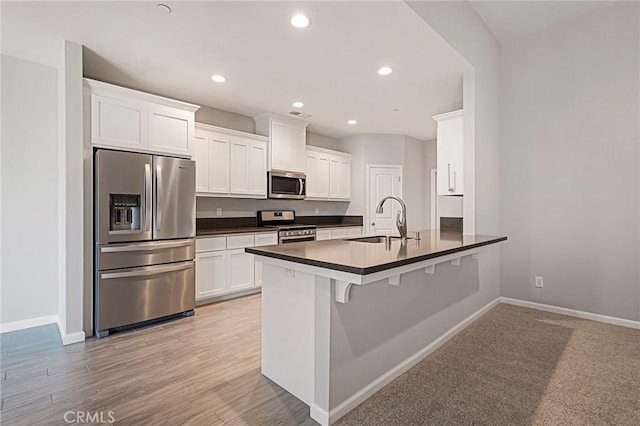 kitchen with appliances with stainless steel finishes, sink, white cabinets, a kitchen bar, and kitchen peninsula