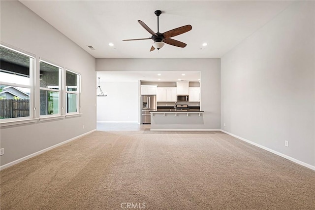 unfurnished living room with ceiling fan, light colored carpet, and sink