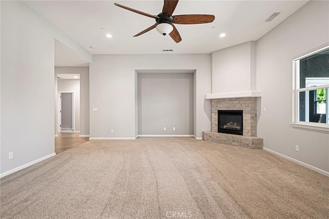 unfurnished living room with ceiling fan, a brick fireplace, and light carpet