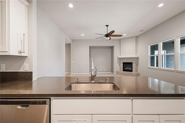 kitchen featuring a stone fireplace, sink, white cabinetry, dishwasher, and ceiling fan