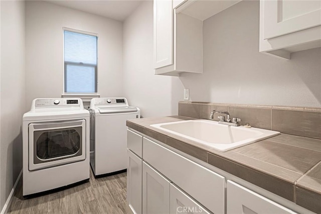 laundry area featuring cabinets, washing machine and dryer, sink, and light hardwood / wood-style flooring