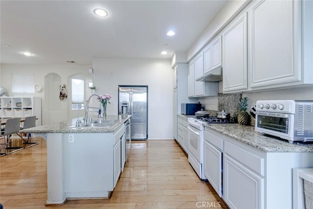 kitchen with sink, white cabinetry, light stone counters, stainless steel appliances, and a kitchen island with sink